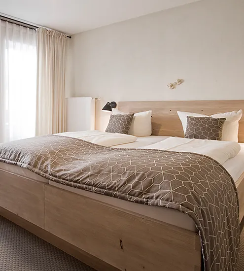 Modernes Hotelzimmer mit Doppelbett, Holzverkleidung und passender Bettwäsche – Einrichtung vom Schreiner nach Maß