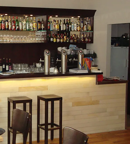 Bar mit heller Holzverkleidung und Rückwandregalen – individuelle Objekteinrichtung für Gastronomie