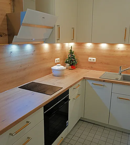 Moderne Einbauküche in L-Form mit Holzarbeitsplatte, weißen Fronten und Dunstabzugshaube – Küchenbau nach Maß.