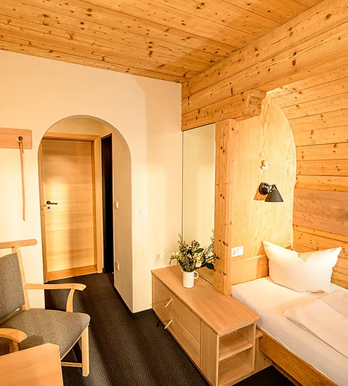 Einzelzimmer mit Holzmöbeln, Wandverkleidung und gemütlicher Sitzecke – individuelle Hotelausstattung