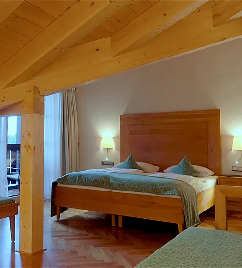 Maßgefertigtes Hotelzimmer mit Massivholzbetten, sichtbarer Holzbalkendecke und indirekter Beleuchtung – eingerichtet von der Schreinerei MH in Eschenlohe
