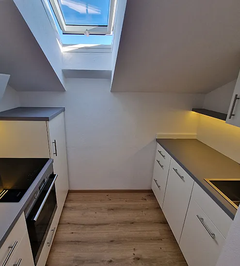 Kompakte Dachschrägenküche mit weißen Schränken und LED-Beleuchtung – platzsparender Innenausbau